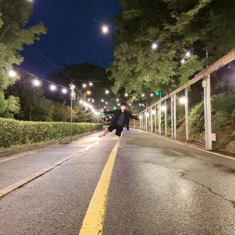 A person down a quiet road under the night sky, illuminated by faint streetlights.